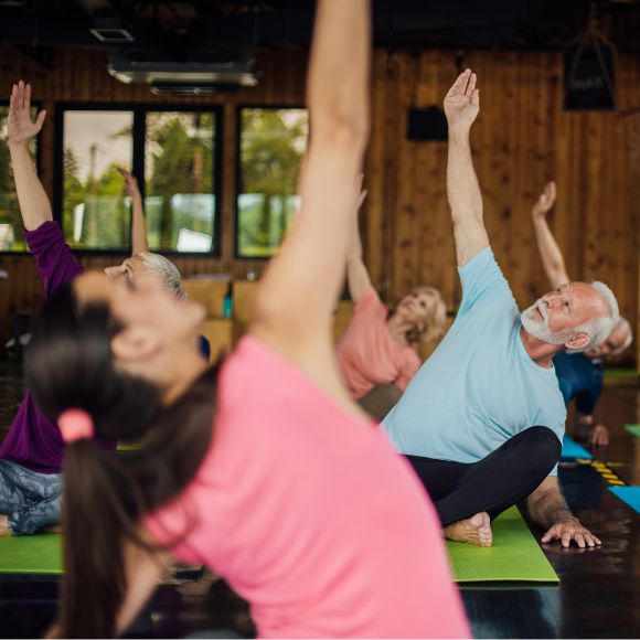 Eine Yoga-Gruppe bestehend aus Männern und Frauen machen gemeinsam Yoga mit einer Trainerin.