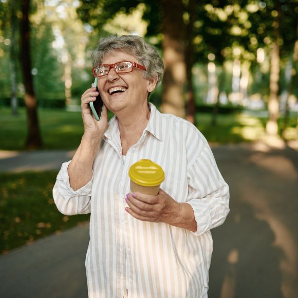 Eine ältere Dame, die lachend mit einem Handy telefonierend spazieren geht.