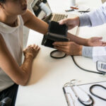 Eine junge Frau ist beim Kardiologen und ihr Blutdruck wird gemessen.